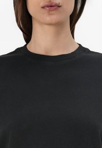 Svart crewneck genser laget av glatt bomullsstoff; har en enkel, sømløs halslinje og en lett løs passform.