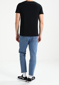 Zwarte T-shirt met korte mouwen, blauwe denim jeans, zwarte sneakers met witte zolen en geribbelde witte sokken. Simpel, ontspannen pasvorm ontwerp.