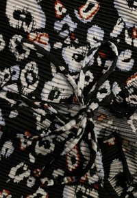Svart tyg med plisserad struktur har ett mönster av vita och gråa skallar, accentuerat av rostfärgade detaljer och en central knytning.