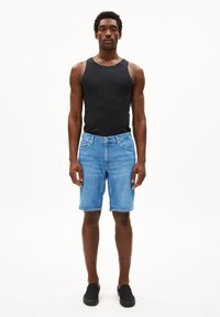 Shorts en denim bleu clair avec poches latérales, coupe droite et coutures visibles. Associés à un débardeur noir et des chaussures noires à enfiler.