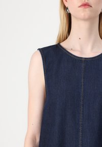 Σκούρο μπλε τζιν φόρεμα με στρογγυλή λαιμόκοψη και χωρίς μανίκια. Διαθέτει ορατές ραφές και ίσια σιλουέτα. Λείος υφασμάτινος τύπος.