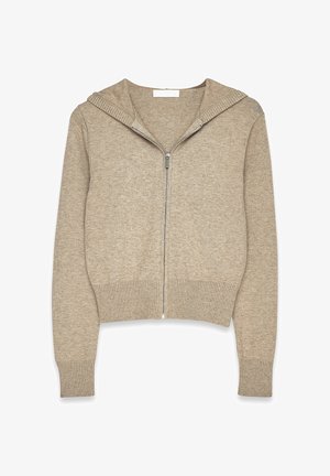 Bežinė zip-up džemperis su raukšlėtu apvadu ir rankovėmis, turintis pamuštą gobtuvą ir lygų paviršių. Tinka kasdieniam dėvėjimui.