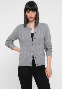 Cardigan grigio a maglia con colletto rotondo, maniche lunghe e chiusura con bottoni. Presenta polsini e orlo a coste. Logo dettagliato in modo sottile.