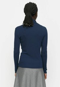Navy long-sleeve top with a fitted design and ribbed texture, featuring a high collar and seamless shoulders, paired with a grey skirt.