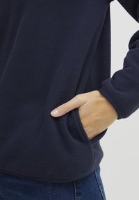 Tumesinine fliispullover pehme tekstuuriga, küljetasku ja elastsete mansettidega. Mõeldud mugavuseks ja soojuseks.