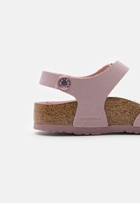 Růžová sandál Birkenstock s texturovaným páskem a korkovou stélkou. Obsahuje kulatou tlačítkovou značku a gumovou podrážku.