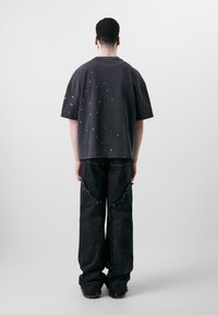 Lõtv must puuvillane t-särk, mille seljal on väikesed metallist praatlised. Koos mustade kulunud laia säärega teksadega, millel on lõhenenud servad.