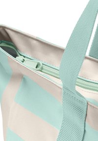 Närbild av en beige och ljus teal randig tote-väska med matchande teal dragkedja och slitstarka vävda handtag.