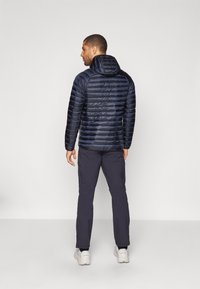 Mornarska puffer jakna s horizontalnom quilted teksturom, pričvršćenim kapuljačom i elastičnim manžetama, u kombinaciji s mornarskim hlačama i bijelim tenisicama.