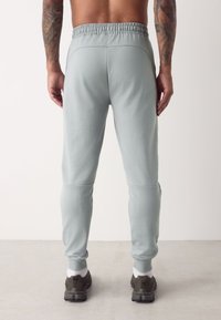 Pantaloni sport verzi deschis, cu talie elastică, pantaloni conici și buzunare laterale, asortați cu adidași închiși la culoare și șosete albe de gleznă.