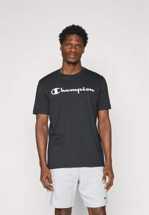 Black cotton T-shirt featuring a white "Champion" logo across the chest. Short sleeves, round neck, displayed with grey shorts.