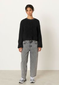 Svart stickad kofta med en fluffig textur, med rund halsringning och knäppning fram, tillsammankopplat med högmidjade grå jeans och sneakers.