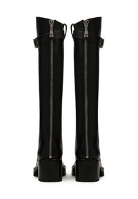 Botas negras hasta la rodilla, hechas de un material suave, con una cremallera central, detalles de correas y tacones gruesos con suelas texturizadas.