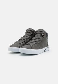 Zapatos deportivos de caña alta en cuero gris oscuro con cordones planos grises, suela de goma blanca y punta redondeada. Presenta ojetes de metal y acentos de costura.