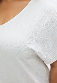 Λευκή υφασμάτινη μπλούζα με διακριτικό σχέδιο με ρυτίδες. Διαθέτει λαιμόκοψη σε σχήμα V και κοντά μανίκια, κατασκευασμένη από ελα φρύ ύφασμα.