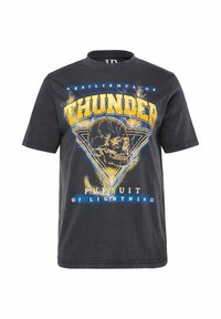 Sort bomuld T-shirt med grafisk tryk af en kranium inden for en trekant, tekst der lyder "Thunder" og "Pursuit of Lightning" med lyn-accenter.