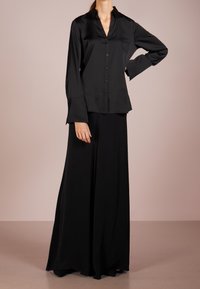 Camicia nera in satin a maniche lunghe con bottone sul davanti, abbinata a una gonna lunga fino al pavimento. Texture liscia e vestibilità comoda.