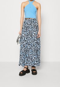 Haut court bleu avec un design croisé associé à une jupe longue et fluide présentant un imprimé animal noir et bleu. Sandales noires épaisses.