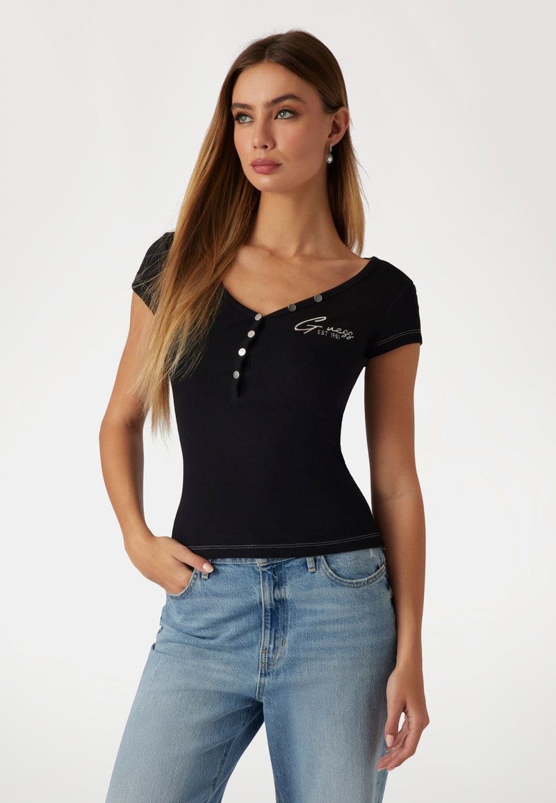 Top preto ajustado com mangas curtas, decote em V, detalhes em botão e logótipo bordado. Combinado com jeans de cintura alta em azul claro.