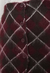 Κοντινό πλάνο μπορντό και σκούρου καφέ argyle πλεκτή ζακέτα με μπορντό κουμπιά και λευκές γραμμές διακριτικά.