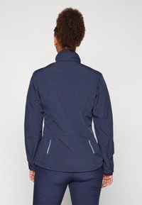 Veste bleu marine avec poches zippées, col montant et tissu texturé. Présente une coupe ajustée avec des détails de couture discrets.