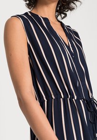 Vestido de marina con rayas verticales beige, sin mangas, escote en V, detalle de botones, cintura elástica y acentos de cordón para un ajuste ajustable.