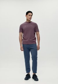 Majica kratkih rukava u mavrinaste boje s suptilnim logotipom, u kombinaciji s plavim trenirkama i crnim tenisicama; glatka tekstura, ležeran kroj.