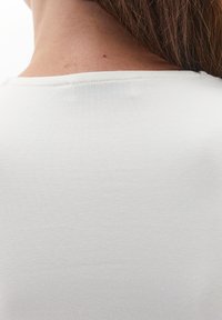 Nuca di una persona con capelli castani che indossa una maglietta bianca a maniche corte, in primo piano sulla pelle e sulla trama del tessuto.