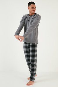 Szürke bolyhos hosszú ujjú felső gombokkal és logóval, fekete és szürke kockás flanelnadrággal párosítva. Cipő nélkül, álló póz.
