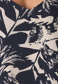 Námořnická modrá a krémová v-neck top s texturovanou tkaninou a velkým listovým vzorem v černé barvě. Vzor obsahuje různé detaily štětcem.