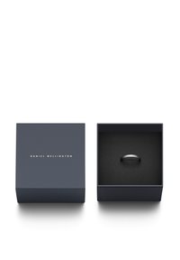 Black ring displayed in a dark, velvet-lined box. Box features a matte navy exterior with gold lettering for "Daniel Wellington."