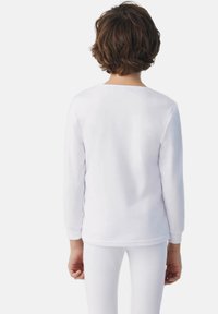 Camisa blanca de manga larga en material suave, con un escote redondeado y un ajuste relajado, combinada con leggings blancos, sin patrones visibles.