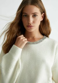 Maglione bianco lavorato a maglia con texture a costine e scollo abbellito da perline. Le maniche sono morbide e leggermente a sbuffo.