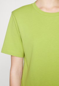 Camiseta de manga corta en algodón verde brillante con un cuello redondo y una textura suave, que presenta un diseño simple y una costura discreta.