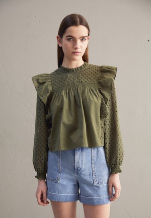 Blouse vert olive avec des épaules volantées, des détails en œillets et un corsage froncé ; associée à un short en denim bleu clair avec des poches à clous.