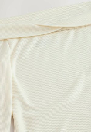Krämfärgad tyg med en vertikal ribbad textur, som har en mjuk drapering och en vikt kant. Slätt, lätt material.