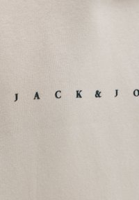 Close-up of beige fabric with text "JACK & J" printed in small, black capital letters on the surface.