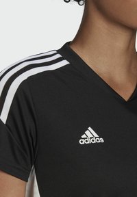 Černé sportovní tričko s výstřihem do V, se třemi bílými pruhy na ramenou a bílým logem Adidas na hrudi. Hladká textura.