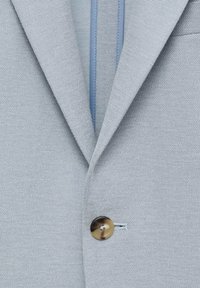 Light gray blazer made of textured fabric. Features a single brown button and a light blue inner lining. Noticeable notch lapels and pocket detail.