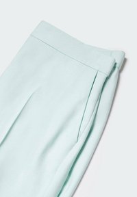 Pantalon bleu clair ajusté plié, montrant la ceinture, la couture latérale et le détail du pli frontal sur un fond neutre.