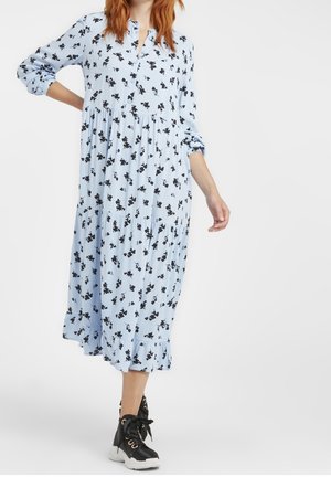 Robe bleu clair avec un motif floral noir, manches longues, patte de boutonnage, design froncé et ourlet à volants. Assortie avec des chaussures montantes noires.