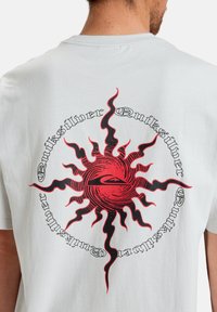 White cotton t-shirt featuring a circular graphic of a red sun with black rays, and "Quiksilver" text in a black stylized font around it.