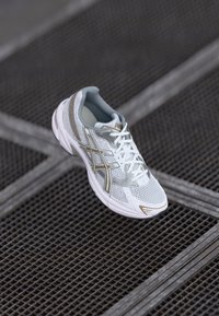 Baskets de sport blanches avec empeigne en mesh, accents argentés et semelle texturée. Présente des lacets et un col de cheville rembourré ; conception légère.