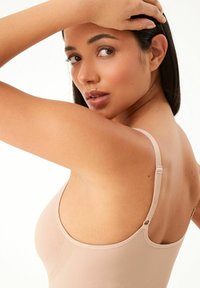 Nude naadloze bodysuit met verstelbare banden, zachte textuur en een aansluitend ontwerp. De stiknaden aan de zijkant voegen detail toe.