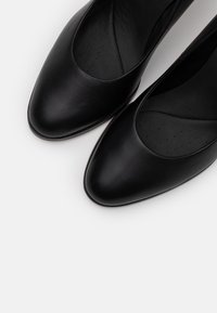 Ballerines en cuir noir avec un bout pointu, une texture lisse et des ouvertures arrondies ; semelles intérieures rembourrées avec de petites perforations pour la respirabilité.