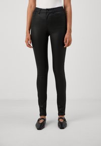 Svarta, stretchiga byxor med smal passform, som har framfickor och en slät, glänsande yta. Bärs med platta, svarta skor.