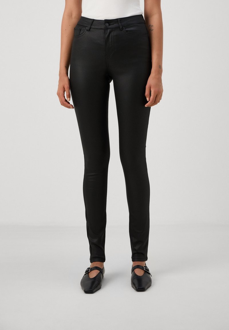 Svarta, stretchiga byxor med smal passform, som har framfickor och en slät, glänsande yta. Bärs med platta, svarta skor.