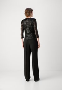 Schwarzes Paillettenoberteil mit Dreiviertelärmeln, tailliert, kombiniert mit hochgeschnittenen schwarzen Hosen; glatte Textur und glänzende Oberfläche.