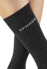 Schwarze, gerippte kniehohe Socken aus einem weichen, strukturierten Material, mit weißem "CPRNCH"-Logo am oberen Rand.
