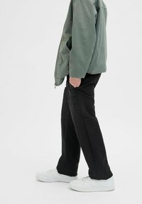 Zelena zip-up jakna, ohlapne črne hlače in bele superge. Obleka ima preprost dizajn brez vidnih vzorcev ali logotipov.
